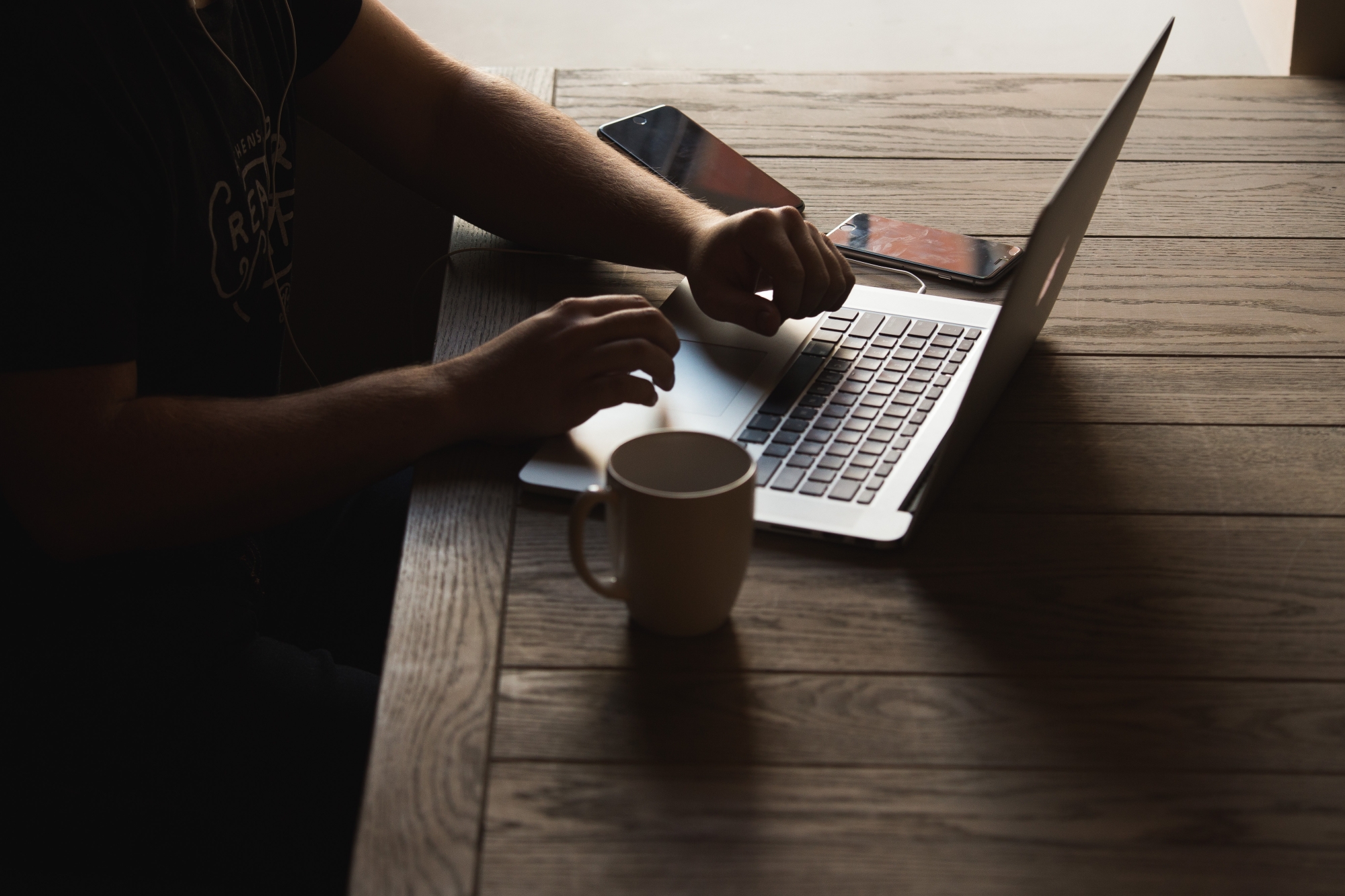 sitting person a mug next to it typing on a macbook